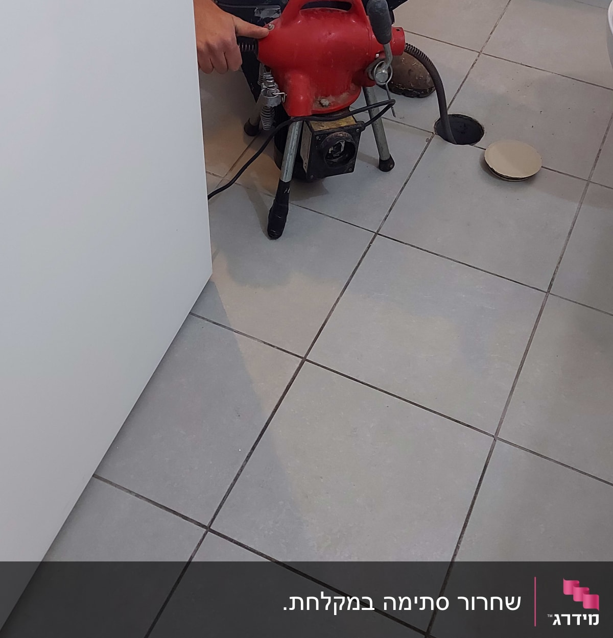 אדם עם כפפות כתומות משתמש במכונת ניקוי צינורות אדומה